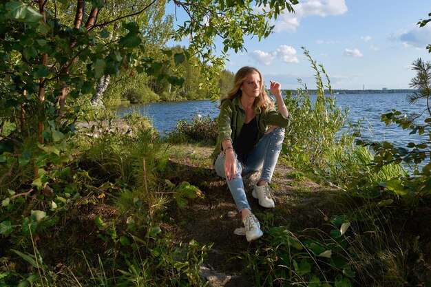 Una chica en jeans en la orilla de un hermoso lago contra el cielo con nubes