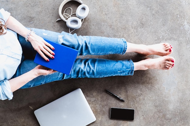 Chica en jeans sentada en el suelo en casa con un bolígrafo y auriculares