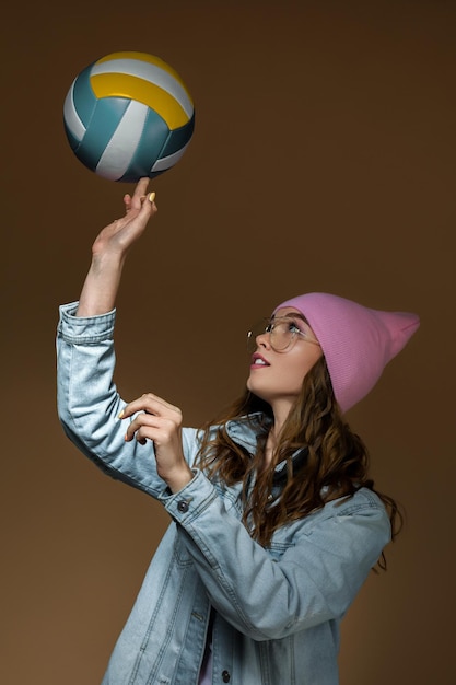 Chica con jeans, un sombrero rosa y gafas elegantes con una pelota