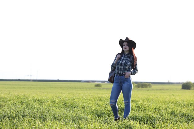 Una chica en jeans y un sombrero viaja el verano en el campo.