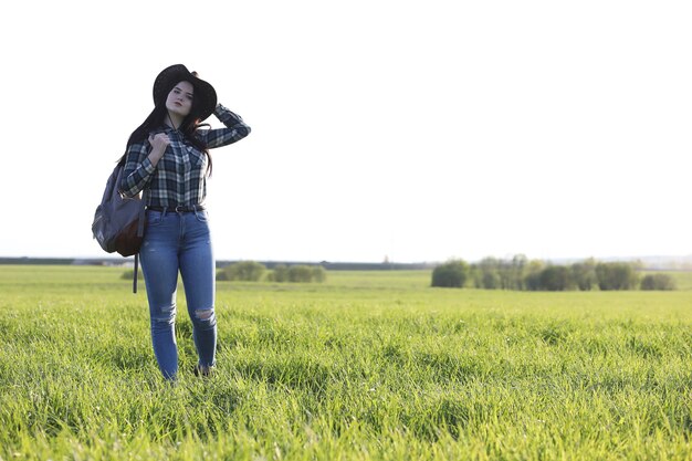 Una chica en jeans y un sombrero viaja el verano en el campo.