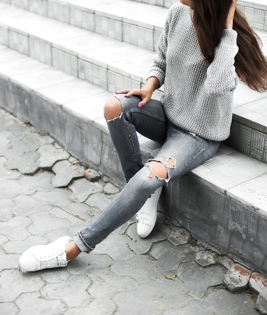 Chica en jeans y suéter sentado en las escaleras