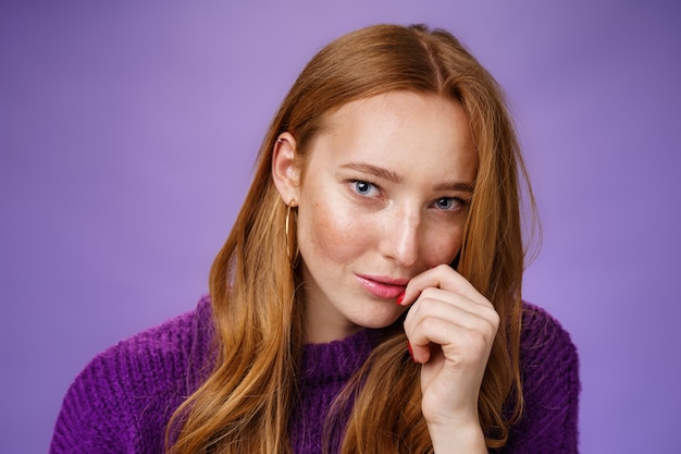 La chica de jengibre encanta con una sensual mirada romántica. Retrato de coqueteo confiado y atractivo pelirrojo mujer inclinando la cabeza tocando los labios y mirando audaz a la cámara contra el fondo púrpura.