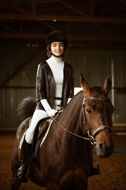 Una chica jockey en traje de gala se sienta en un caballo representado un fragmento del cuerpo de una niña un caballo bozal un br ...