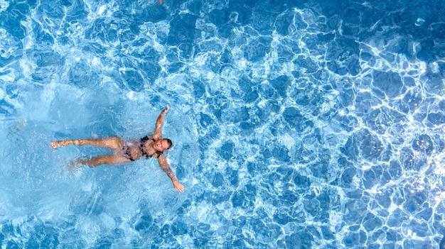 Chica joven activa en piscina vista aérea drone desde arriba joven nada en agua azul