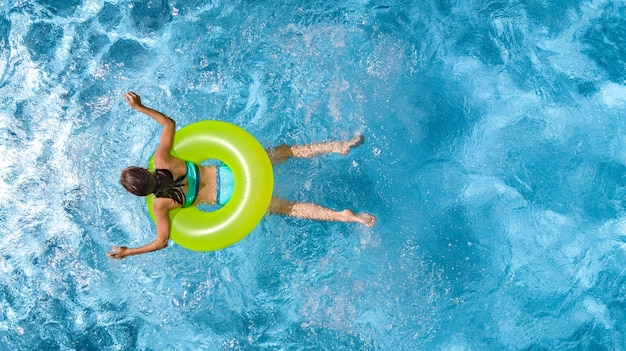 Chica joven activa en la vista superior aérea de la piscina desde arriba niño nada en anillo inflable