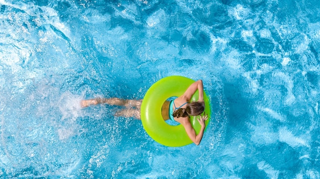 Chica joven activa en la vista superior aérea de la piscina desde arriba niño nada en anillo inflable