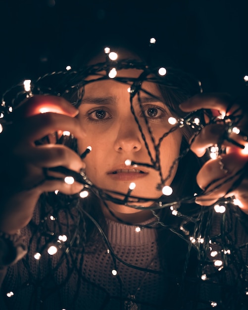 Chica joven agobiada desenredando las luces de navidad