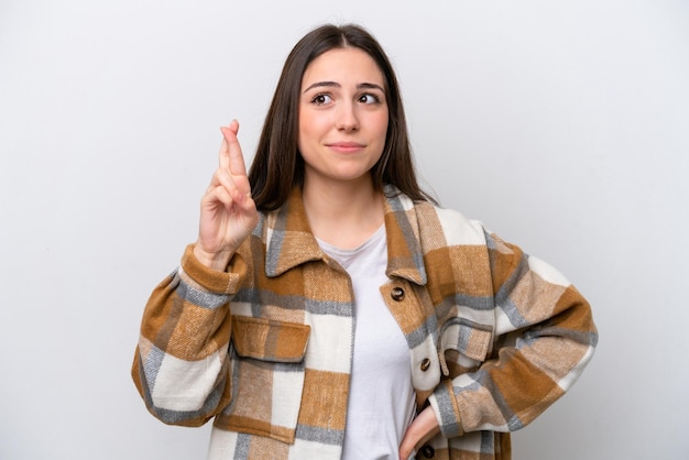 Chica joven aislada sobre fondo blanco con los dedos cruzados y deseando lo mejor