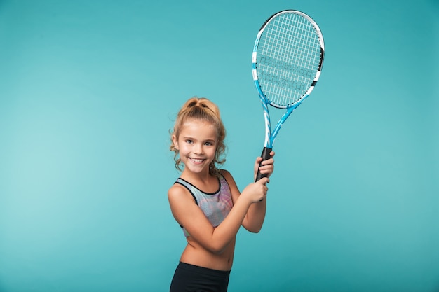 Chica joven alegre deportes jugando tenis aislado sobre pared azul