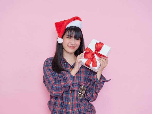 Chica joven alegre con gorro de Papá Noel con cajas de regalo en la pared rosa