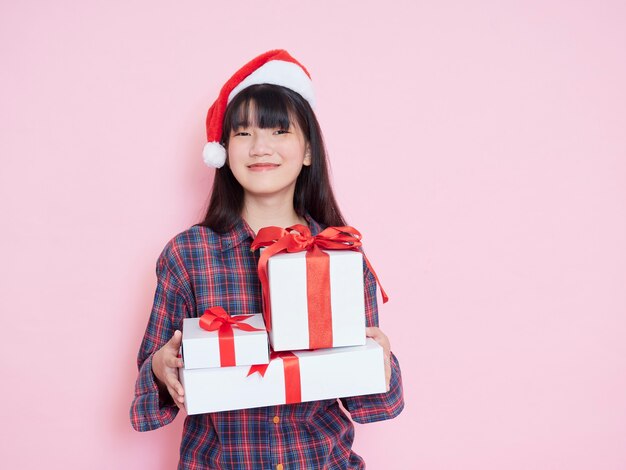 Chica joven alegre con gorro de Papá Noel con cajas de regalo en rosa
