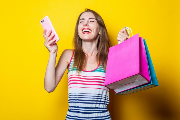 Chica joven alegre con teléfono sosteniendo bolsas de la compra.