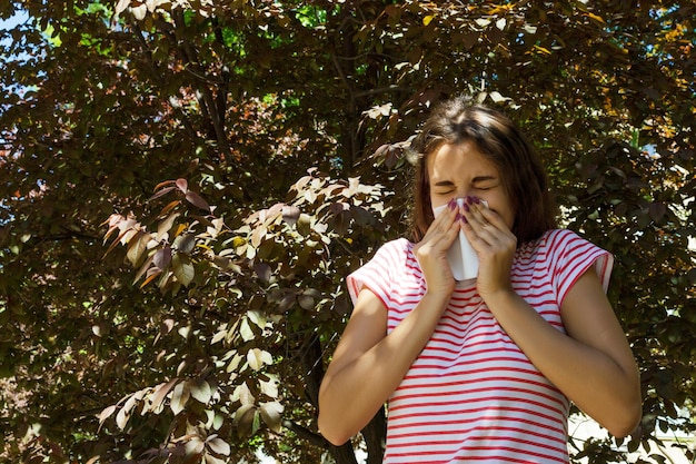 Foto chica joven con alergia en el parque de otoño chica estornuda se suena la nariz en una servilleta