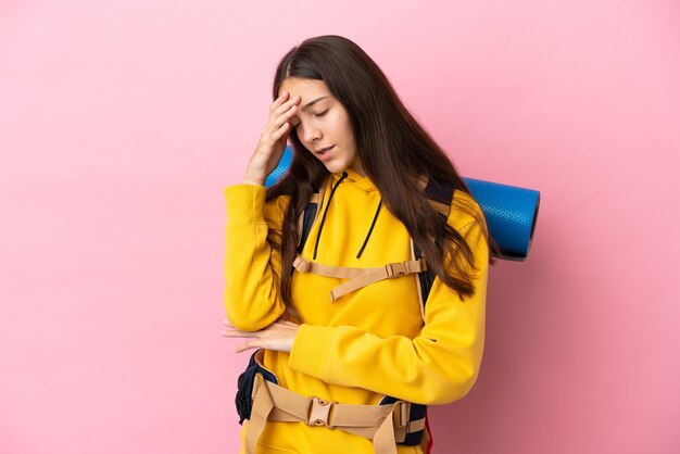 Chica joven alpinista con una mochila grande aislada sobre fondo rosa con dolor de cabeza