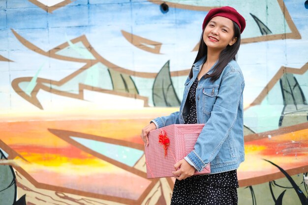 Chica joven asiática con caja de regalo en colores de fondo