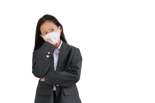 Chica joven asiática usa camisa formal, traje de estudiante y mascarilla protectora usando y mantiene los brazos cruzados y pensando posando con mirando hacia arriba aislado sobre fondo blanco.