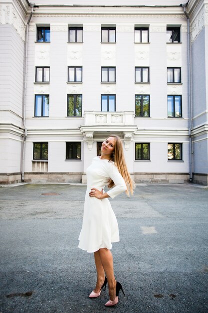 Chica joven de aspecto europeo con un vestido blanco en el fondo del edificio.