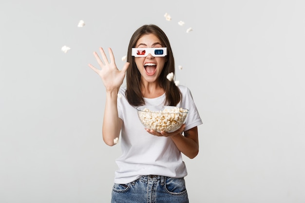 Chica joven atractiva alegre en gafas 3d, lanzando palomitas de maíz en la pantalla mientras ve la película.