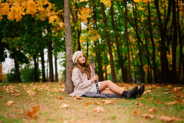 Chica joven atractiva con clarinete, ébano en el parque de otoño