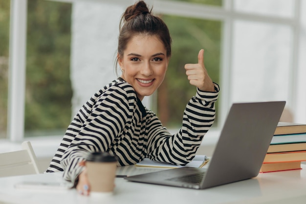 Chica joven atractiva está trabajando en una computadora portátil El estudiante está mirando a la cámara