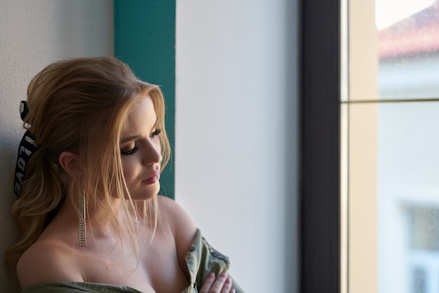 Chica joven atractiva con el pelo recogido. Foto de una chica rubia con piel perfecta en una pared gris