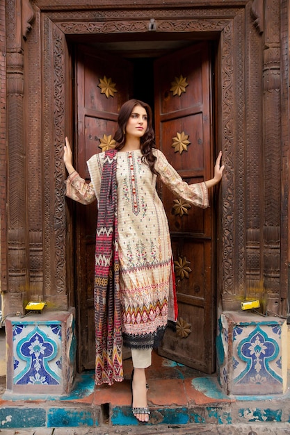 Chica joven atractiva posando con confianza con la puerta de madera vieja para sesión de moda en el lugar antiguo