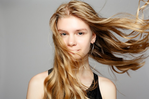 Chica joven atractiva tocando su rostro. Foto de chica rubia con piel perfecta sobre fondo gris. Concepto de belleza y cuidado de la piel. Hermosa mujer joven con maquillaje natural y piel limpia