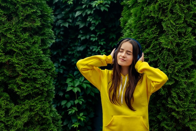 Chica joven en auriculares inalámbricos en el fondo de árboles de Navidad verdes escuchando música