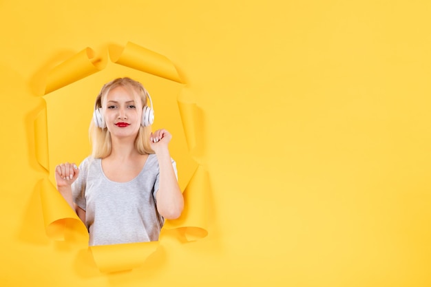 Chica joven en auriculares sobre superficie de papel amarillo rasgado