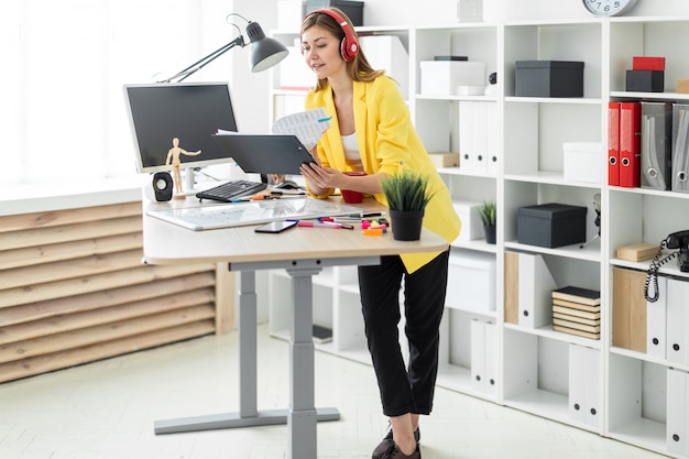 Chica joven en auriculares trabajando con documentos y bebiendo de una taza roja