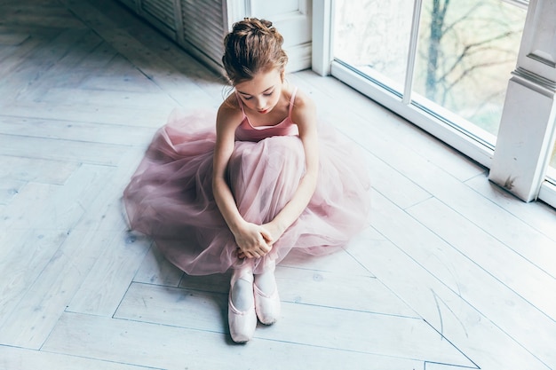 Chica joven bailarina de ballet clásico en clase de baile. Hermosa bailarina elegante en falda tutú rosa se pone zapatos de punta