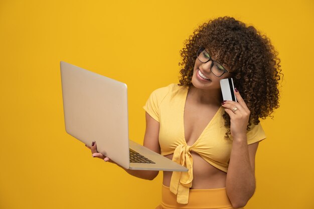 Chica joven y bella de cabello rizado con laptop y tarjeta de crédito