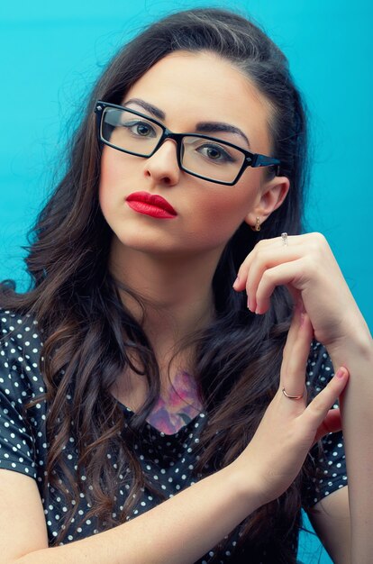 Chica joven y bella en gafas y con maquillaje aislado en la pared azul