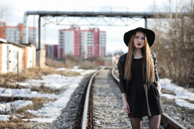 Chica joven y bella con un sombrero y con un exterior de maquillaje oscuro. Chica de estilo gótico en la calle. Una niña camina por las calles de la ciudad con un chaleco de cuero y un teléfono.