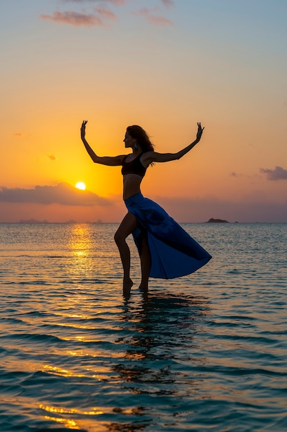 Chica joven belleza bailando en la playa tropical en el agua de mar en la isla paradisíaca al atardecer, de cerca. Concepto de verano. Viajes de vacaciones.