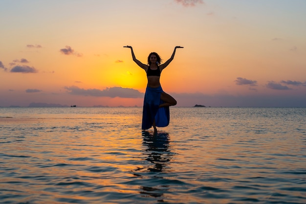 Chica joven belleza bailando en la playa tropical en el agua de mar en la isla paradisíaca al atardecer, de cerca. Concepto de verano. Viajes de vacaciones.