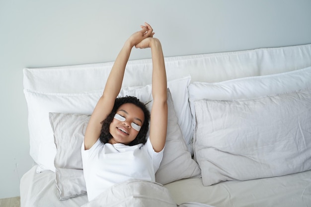 Chica joven con belleza hidratante debajo de los parches para los ojos se estira en la cama Cuidado de la piel amor propio bienestar