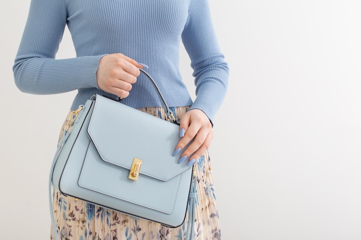 Foto chica joven en blusa azul y falda plisada con bolso azul sobre fondo blanco.