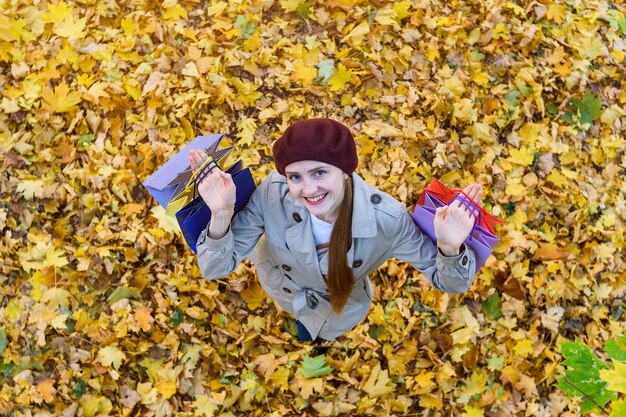 Chica joven con bolsas de compras en las manos en hojas de otoño abackground Vista superior
