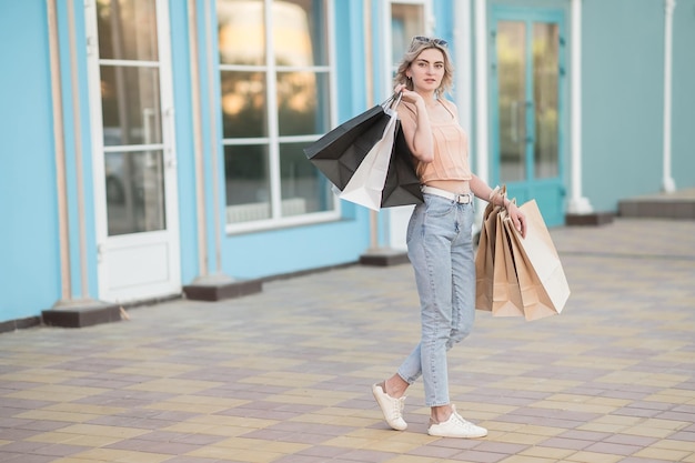 Foto una chica joven con bolsas en vaqueros sale de la tienda de compras al aire libre en verano