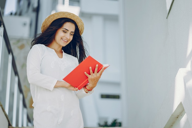 chica joven y bonita en una ciudad de verano de pie cerca de las escaleras con el libro rojo