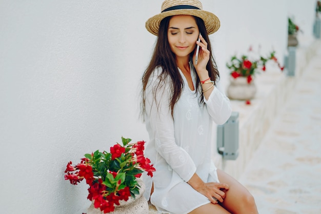 chica joven y bonita en una ciudad de verano sentada cerca de flores con teléfono inteligente