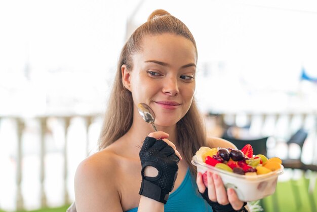 Chica joven bonita deporte sosteniendo un plato de fruta al aire libre