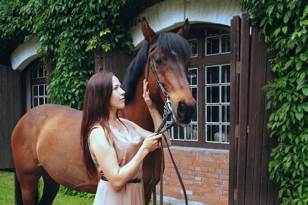 Chica joven con un caballo en el fondo de la ventana de un viejo establo