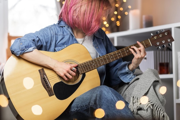 Chica joven de cabello rosado tocando la guitarra en casa