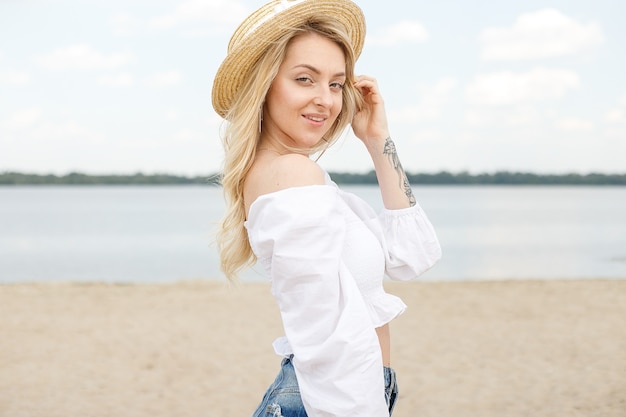 Chica joven con cabello rubio y sombrero de paja en la playa