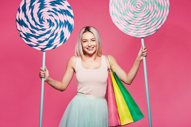 Chica joven con cabello rubio vistiendo top y falda de pie con enormes paletas dulces