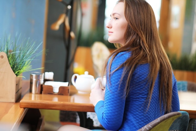 La chica joven en el café se sienta y bebe té