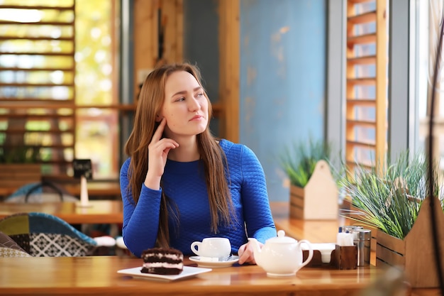 Chica joven en la cafetería se sienta y bebe té con postre